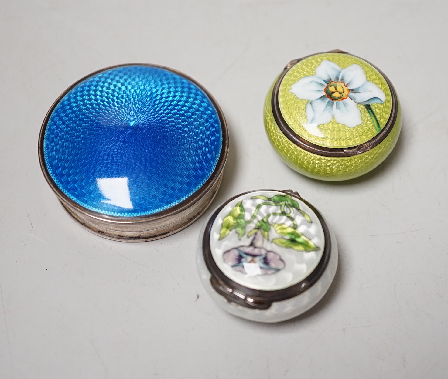 An Edwardian Art Nouveau silver and enamel pill box, import marks for London, 1901, one other 900 standard and enamel pill box and silver and enamel compact, largest 52mm.